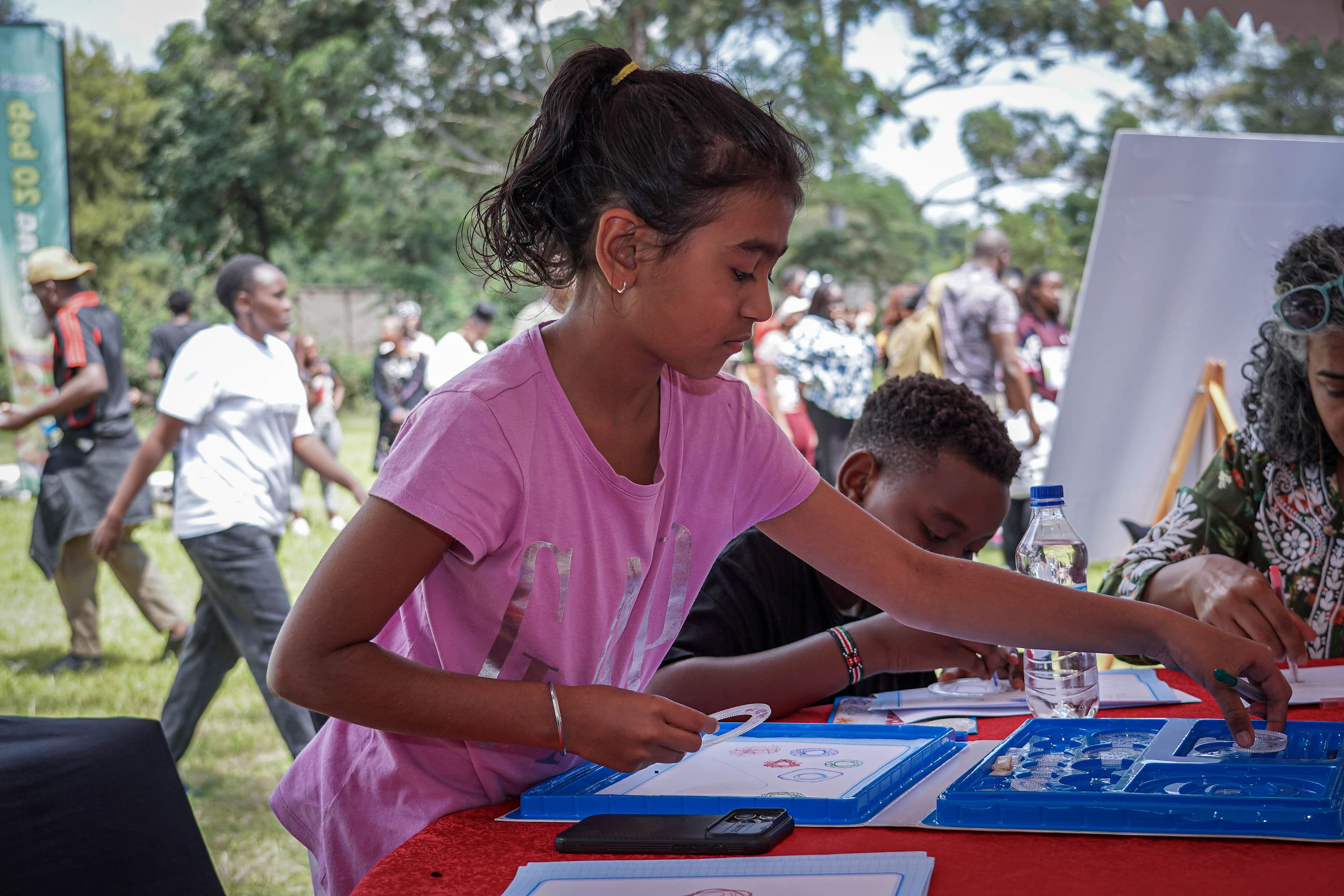 A girl working on a circle-drawing puzzle at a table outdoors