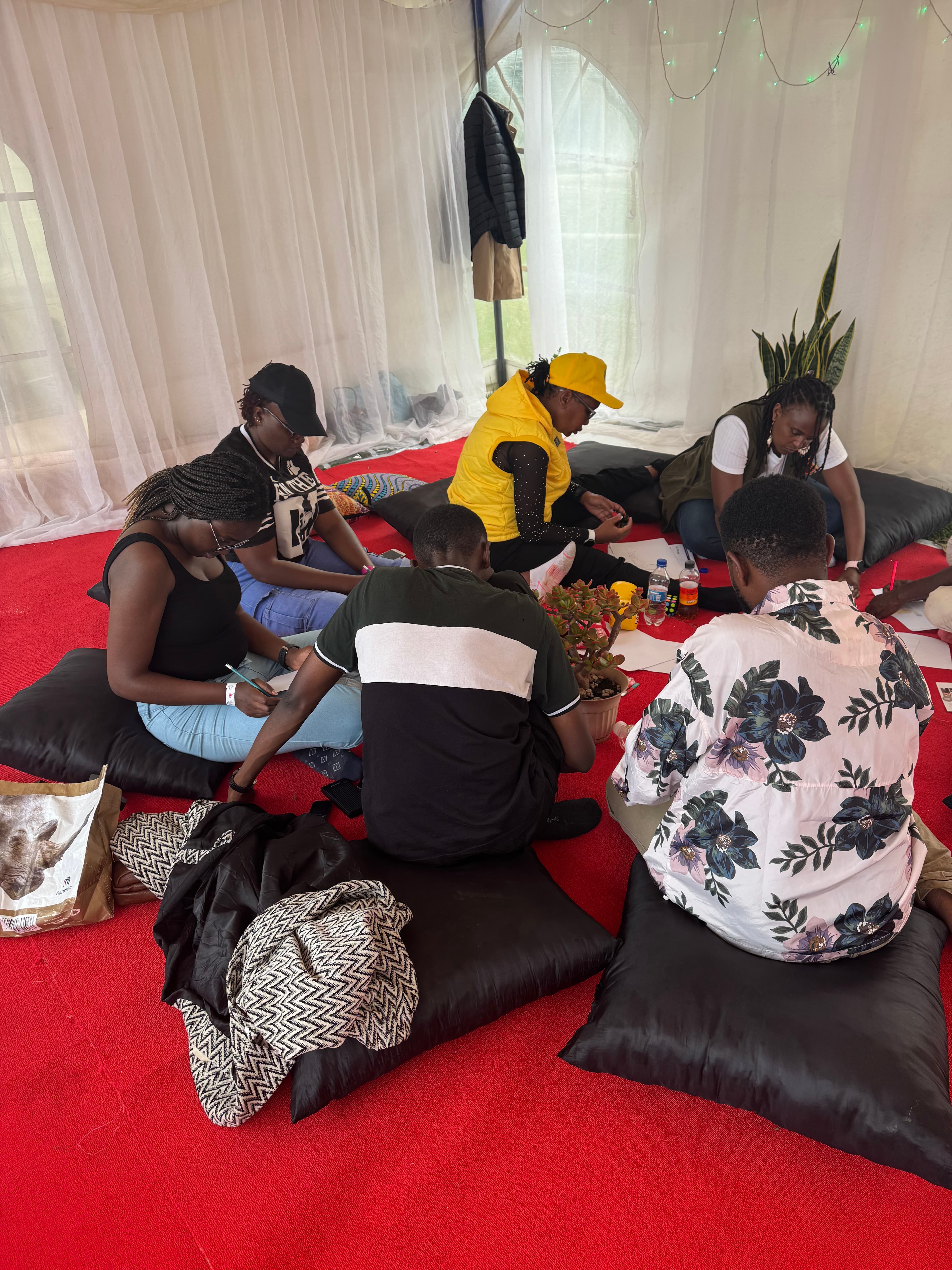 A small group sitting on cushions in a tent, writing and reflecting together