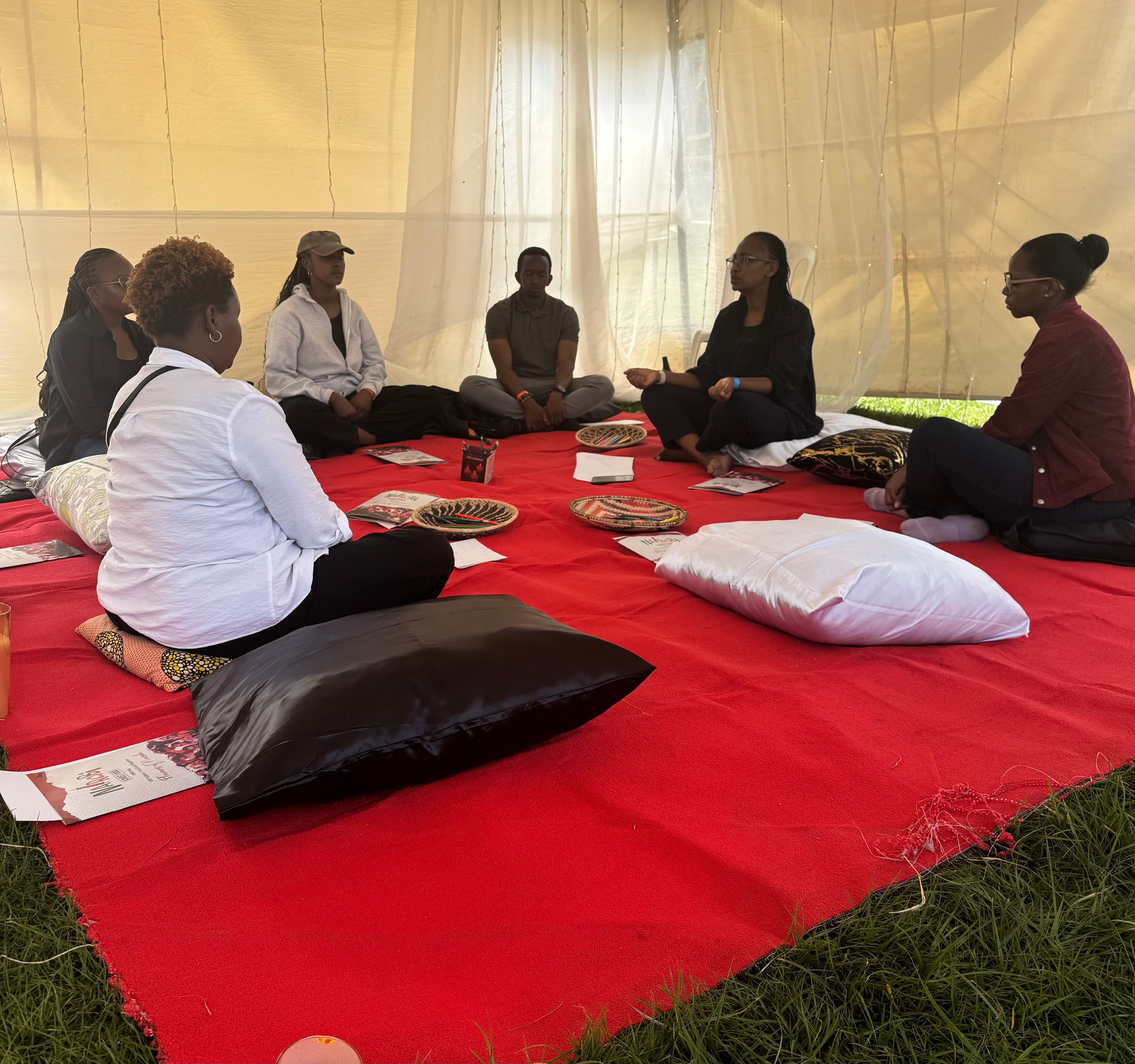 A facilitator leading a seated circle of participants in a warm tent setting