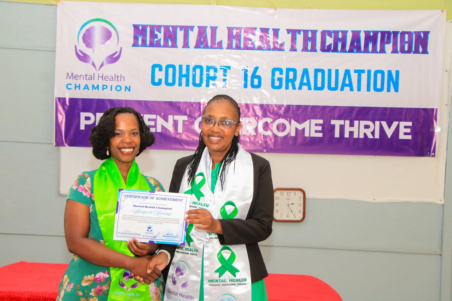 A Mental Health Champion graduate holding a certificate beside a mentor at Cohort 16 graduation