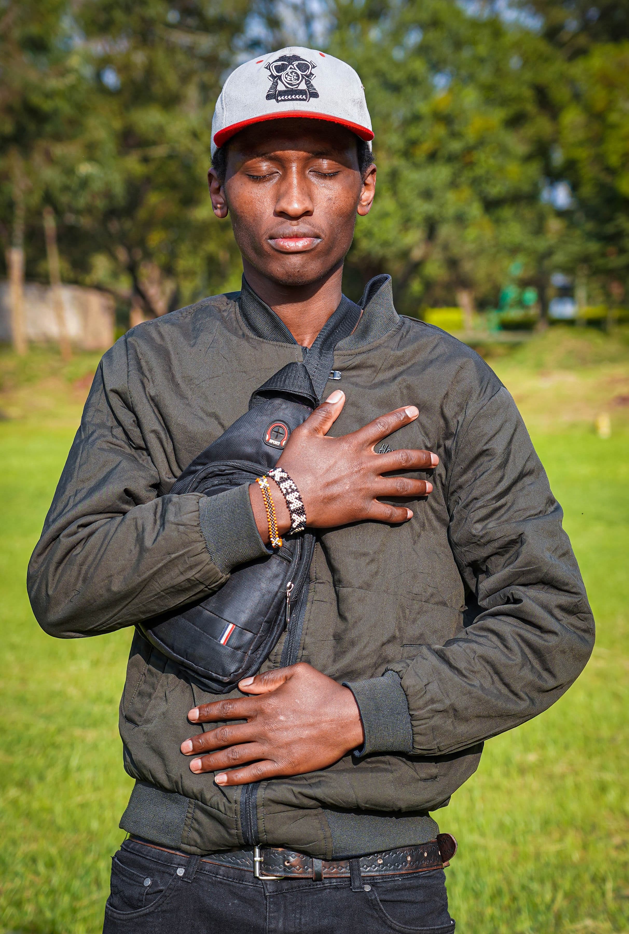 A man standing outdoors with his eyes closed and hands resting on his chest